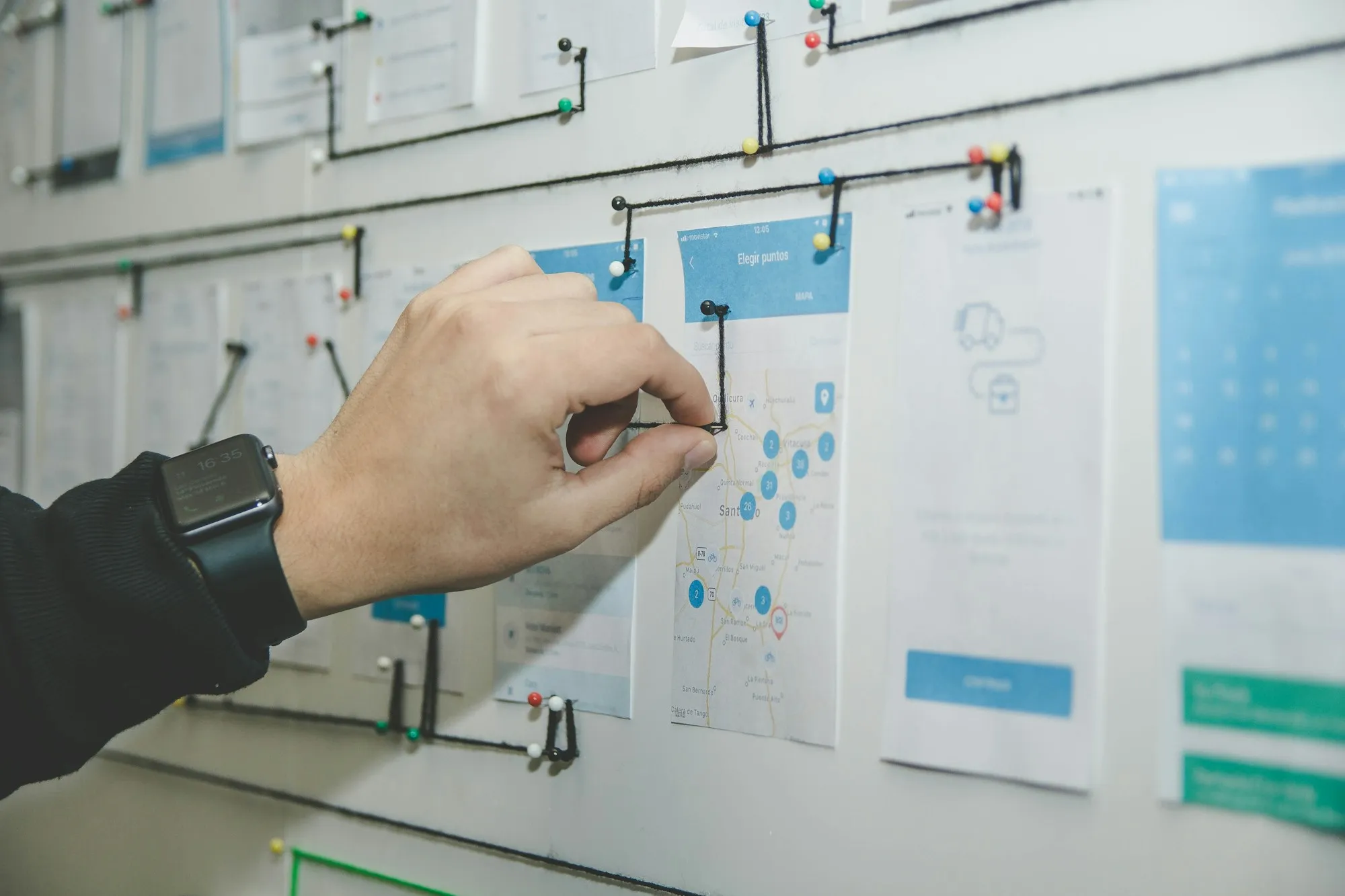 A hand pinning a user flow between app screens on a planning wall